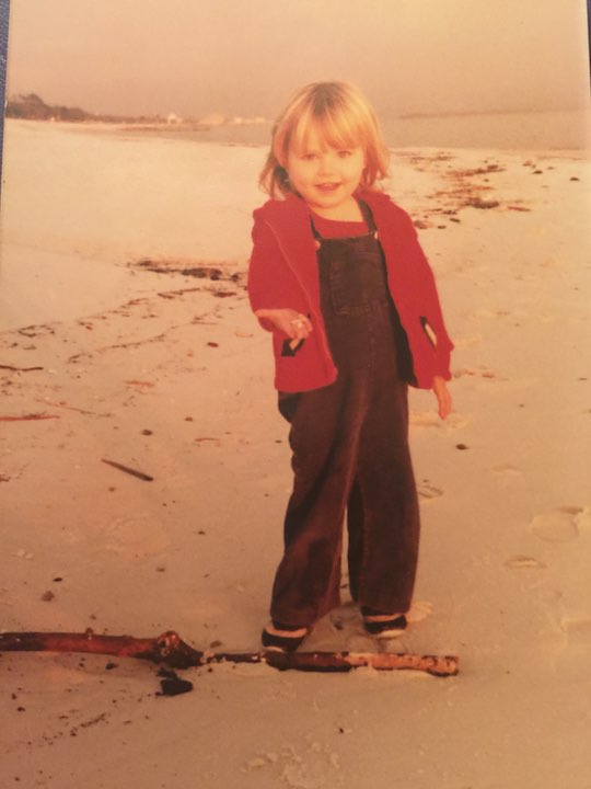 A young Harmony Eichsteadt smiling standing on the beach holding out her hand