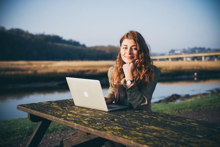 Natalia Komis profile smiling with laptop on picnic bench by river
